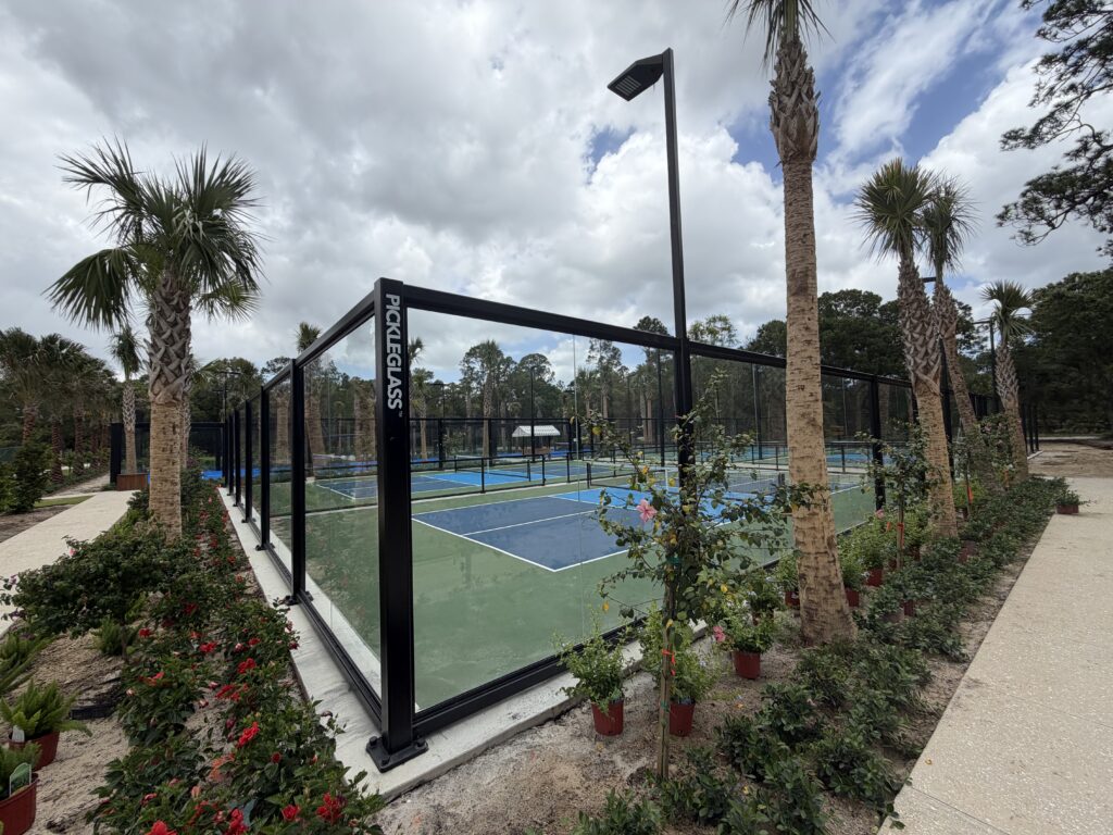 Acoustic-rated structural glass pickleball enclosure installed near residential units to mitigate noise for neighbors.