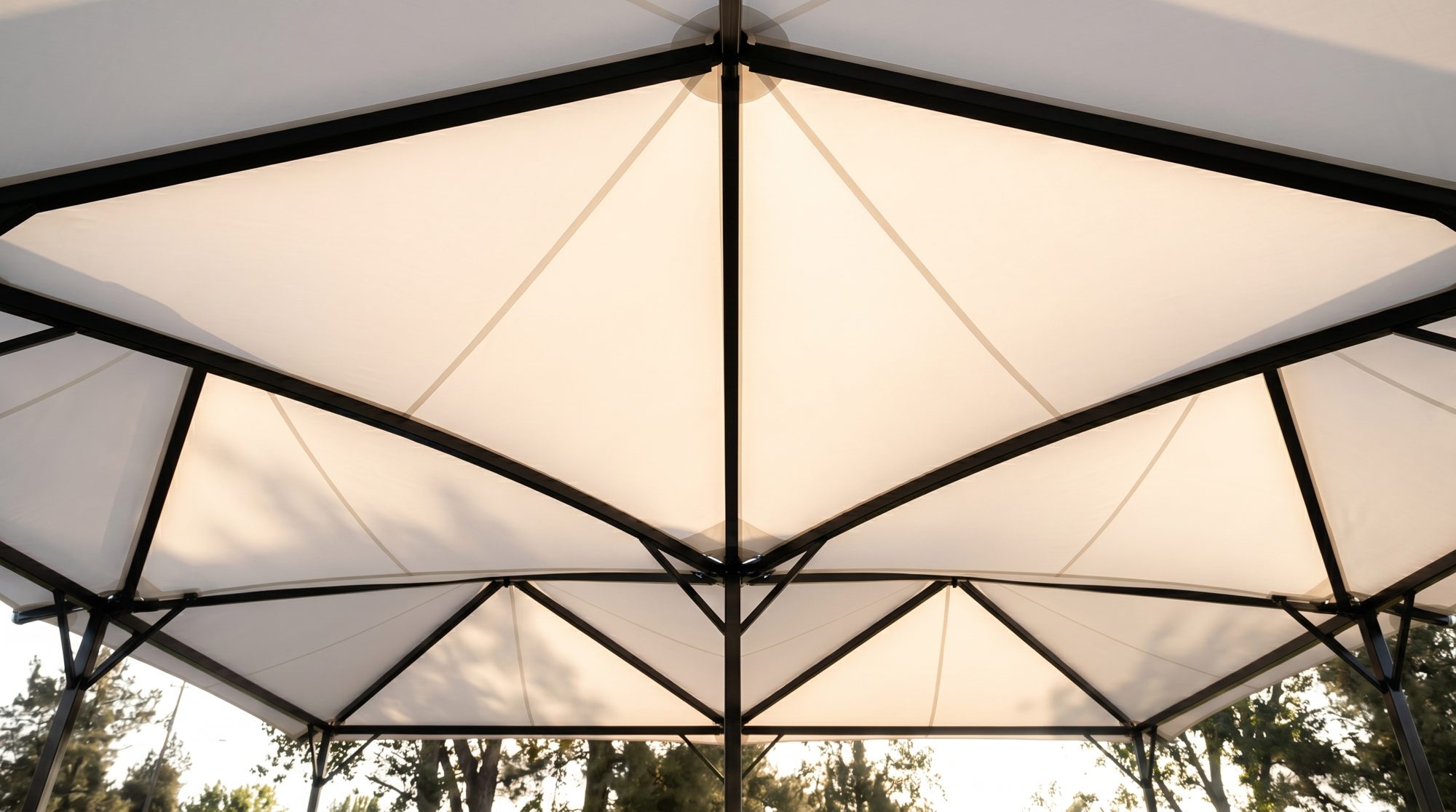 Daylight diffused through a white PTFE tensile membrane canopy over a racquet court, soft and even with no harsh glare